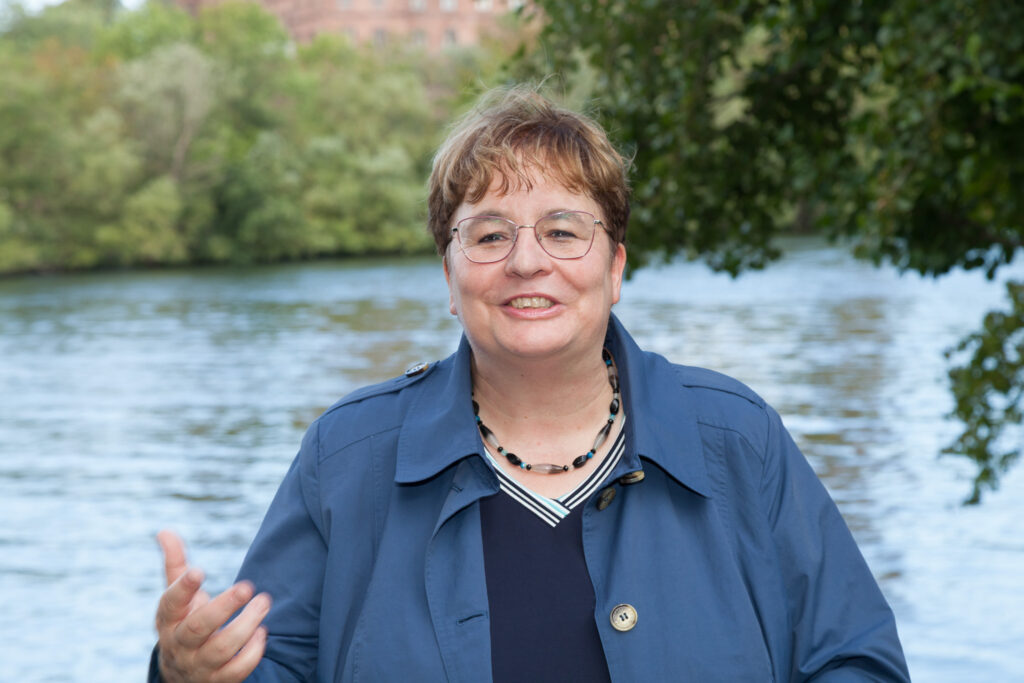 Frau Dr. Schliessmann lädt ein, ins Gespräch zu kommen. im Hintergrund sieht man den Main.